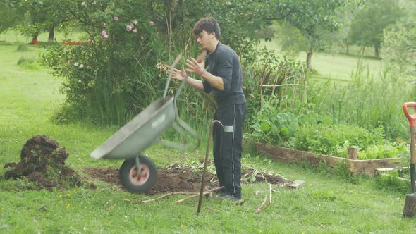 Young male gardener tipping wheelbarrow tending to garden