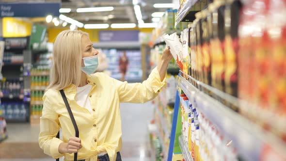 Beautiful Woman Standing Near Shelf With Goods Looks Carefully on Every Products