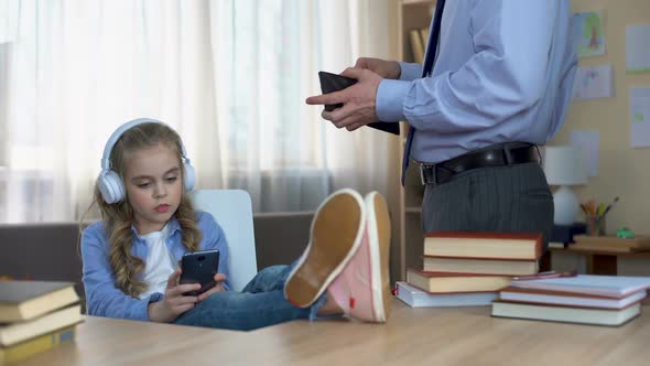 Father in Suit Giving Pocket Money to Daughter Listening to Music in Headphones