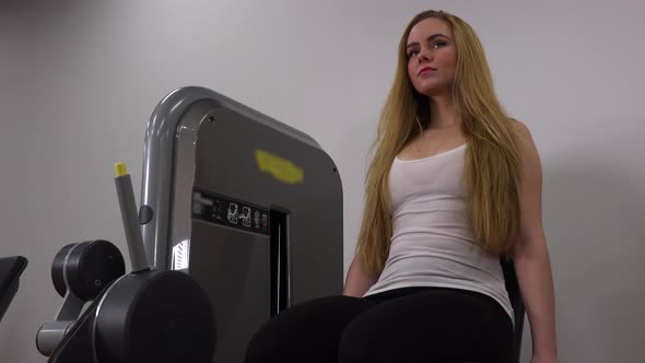 A Young Beautiful Woman Trains Legs on a Machine in a Gym - Closeup From Below