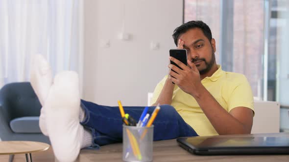 Indian Man with Smartphone Resting Feet on Table