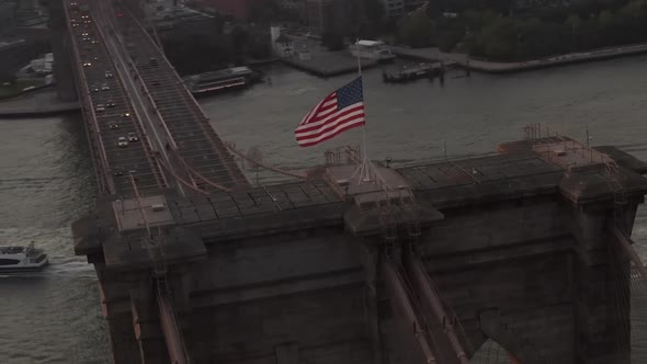 AERIAL: Close Up Circle Flight Over Brooklyn Bridge with American Flag and East River View Manhattan