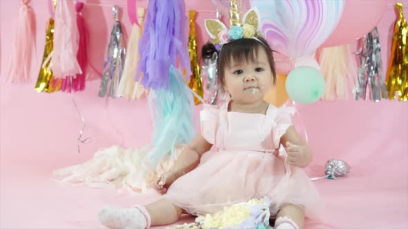 Cute Toddler Eating and Playing with Birthday Cake in Pink Background with Balloons and Decorations