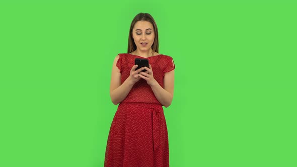 Tender Happy Girl in Red Dress Is Texting on Her Phone. Green Screen