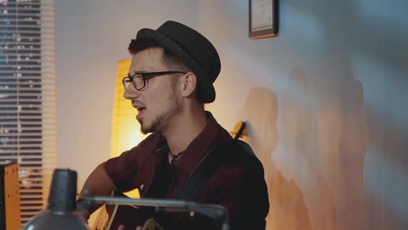 Close-up of Young Musician Singing Into Microphone and Playing the Guitar in Home Recording Studio