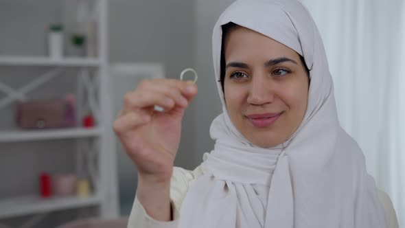 Gorgeous Young Middle Eastern Woman with Hazel Eyes in White Hijab Admiring Engagement Ring in Hand