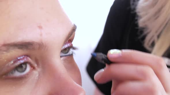 Professional Stylist Makeup Artist Applies a Turquoise Eyeliner Pencil While Making a Bright Evening