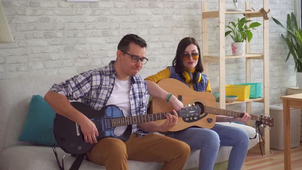 Portrait of Young Woman and Young Man Emotionally Playing Guitars Sitting on Sofa