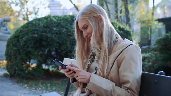 Beautiful Girl on a Bench in Your Phone Looking Photos. Cool Autumn Park. Soft Sunlight