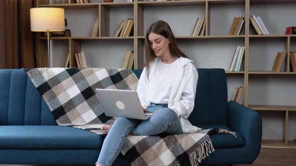 Beautiful Cheerful Girl Using Silver Laptop While Sitting on Sofa in Living Room at Home