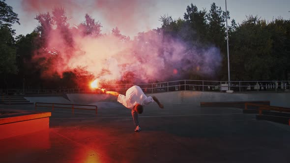 Young Man is Holding Glowing Red Signal Flare Jumping and Spinning While Performing Break Dance on