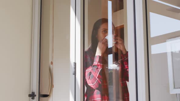 Mixed race woman drinking a cup of coffee standing by window