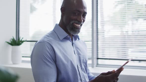 Smiling african american businessman using digital tablet and standing by window in office