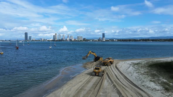 Heavy machinery working on a coastal rejuvenation project with a city skyline in the distance. Panor