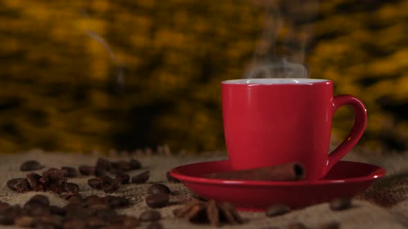 Cup of Coffee with Cinnamon and Beans Scattered on the Table. Blurred Background