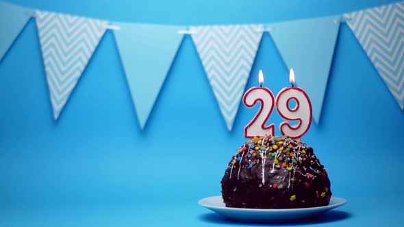 chocolate birthday cake with a burning candle number twenty nine, 29 on a blue background. Copy spac