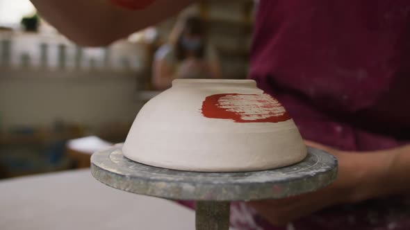 Close up view of female potter wearing apron painting pot on potters wheel at pottery studio