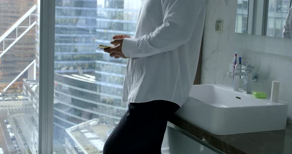 Man Is Walking in Bathroom of Flat in Penthouse with Large Panoramic Windows, Holding Smartphone