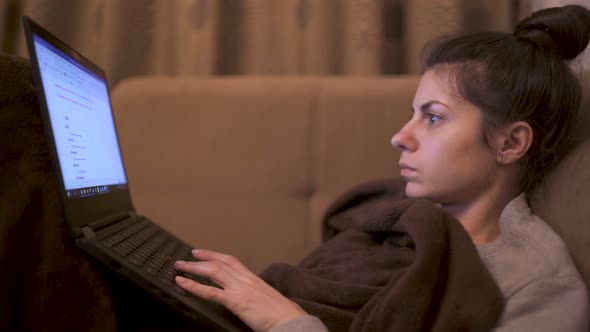 Young Woman Covered with Brown Blanket Working on Laptop From Home During Quarantine