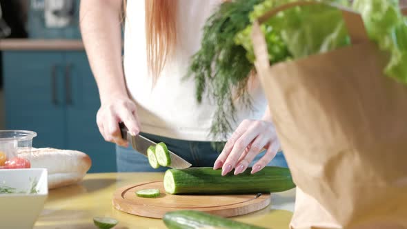 woman in the kitchen on the table cuts ripe cucumbers for a vegetable salad