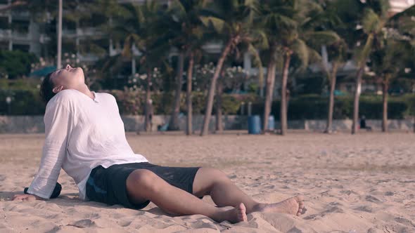 Guy in White Shirt Rests on Ocean Beach Against Palm Trees