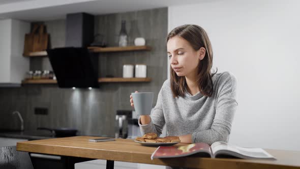 Young Woman Reading Magazine Near Cup at Table 