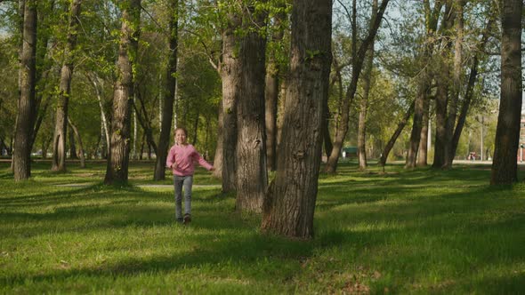 Smiling Little Girl Jumps and Runs Along Lush Grass in Park