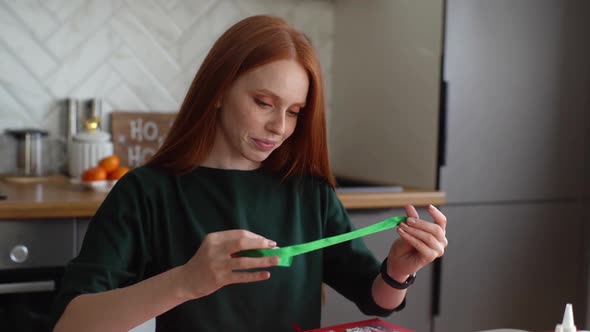 Hand Held Shot of Cheerful Attractive Young Woman Choosing Holiday Ribbon to Frame Board with Advent
