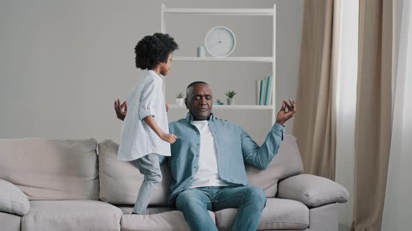 Mature Tired Man Sitting on Sofa in Room Meditating Funny Active Little Daughter Jumping on Couch