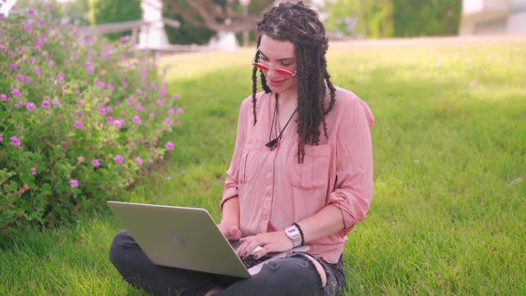 Attractive Woman with Dreadlocks Working at the Laptop Sitting Grass in City Park