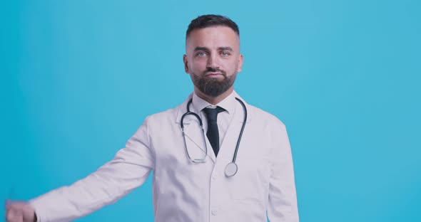 Studio Portrait of Skeptical Medical Doctor Gesturing Thumbs Down with Both Hands, Blue Background