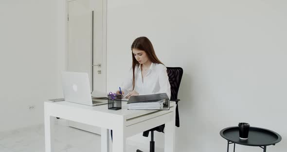 Pretty Student Writing in Notebook When Working with Laptop at Table in Office