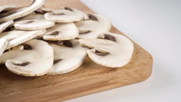 Sliced champignon mushrooms on a cutting wooden board on a white table