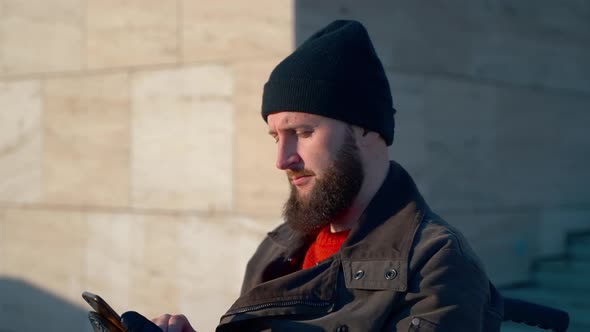 Handicapped Man in Wheelchair is Using Smartphone in City Typing Message in Online Chat