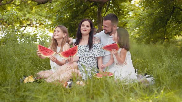 Cheerful Parents with Daughters in Summer Outfits Sitting Together at Green