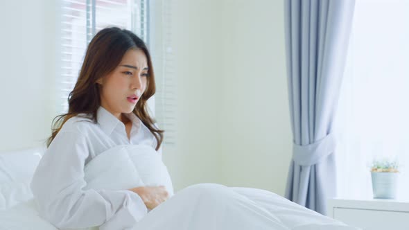 Asian beautiful sick girl in pajamas getting up from sleep in bedroom.