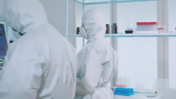 Biochemists Nurse in Protection Suit Bringing Test Tubes
