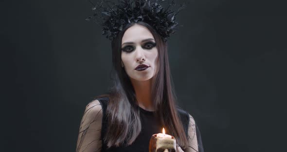 Mystical Female in Black Attire Holds a Skull with a Burning Candle and Looking at the Camera, the