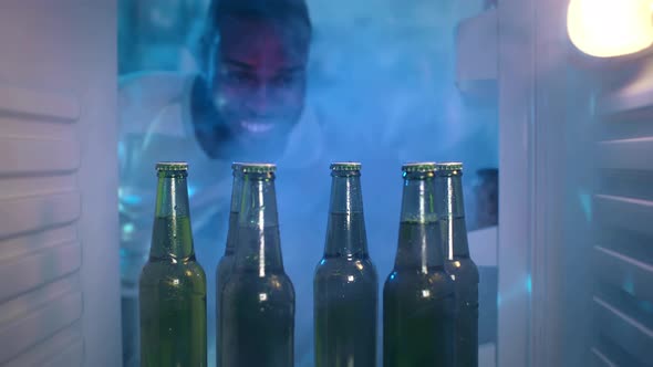 Young AfricanAmerican Ethnicity Man Taking Beer From Fridge Having Party at Home