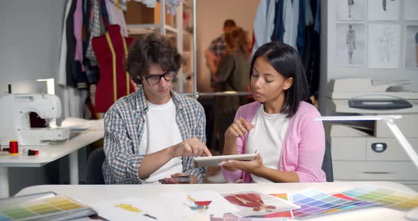 Diverse Designers Discuss on Digital Tablet Sitting at Desk in Workshop