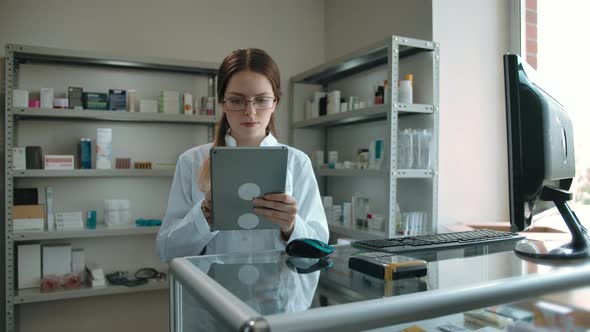 Smart Girl Pharmacists in Glasses with an Electronic Tablet in a Pharmacy
