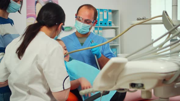 Stomatologist with Mask and Gloves Using Drill Tool for Cleaning Teeth of Kid