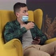 Man Sits in a Chair and Uses a Phone with a Medical Mask  and After Being Asked - VideoHive Item for Sale