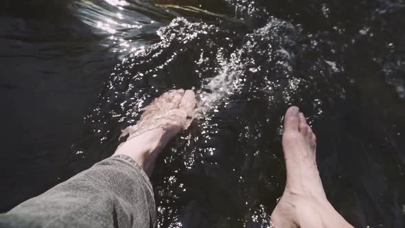 Man Relaxes By River Sitting on Edge of Rock Swing One's Feet on Water Flow