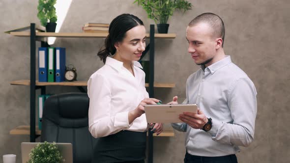 Man and Woman Look at Screen of Tablet and Lead Discussion