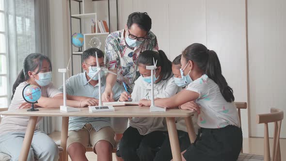 Wearing Facemasks, Enthusiastic Asian Teacher Explains To Young Children How Wind Turbines Work