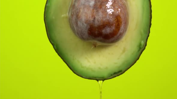 Oil drops falling from avocado on yellow background. Avocado slice and water splashing, drops