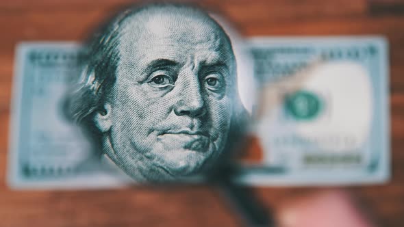 One Hundred Dollars Inspects Under Magnifying Glass on Wooden Table