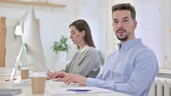 Young Creative Man Working on Desktop and Smiling at the Camera