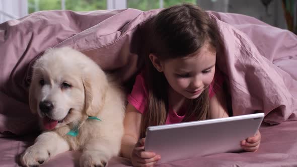 Child Watching Cartoon with Little Dog Pet in Bed alt